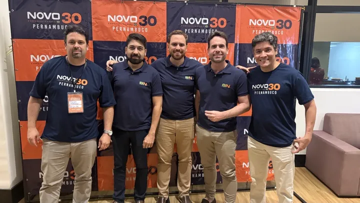 Cinco homens com camisas do NOVO diante do painel NOVO 30 Pernambuco